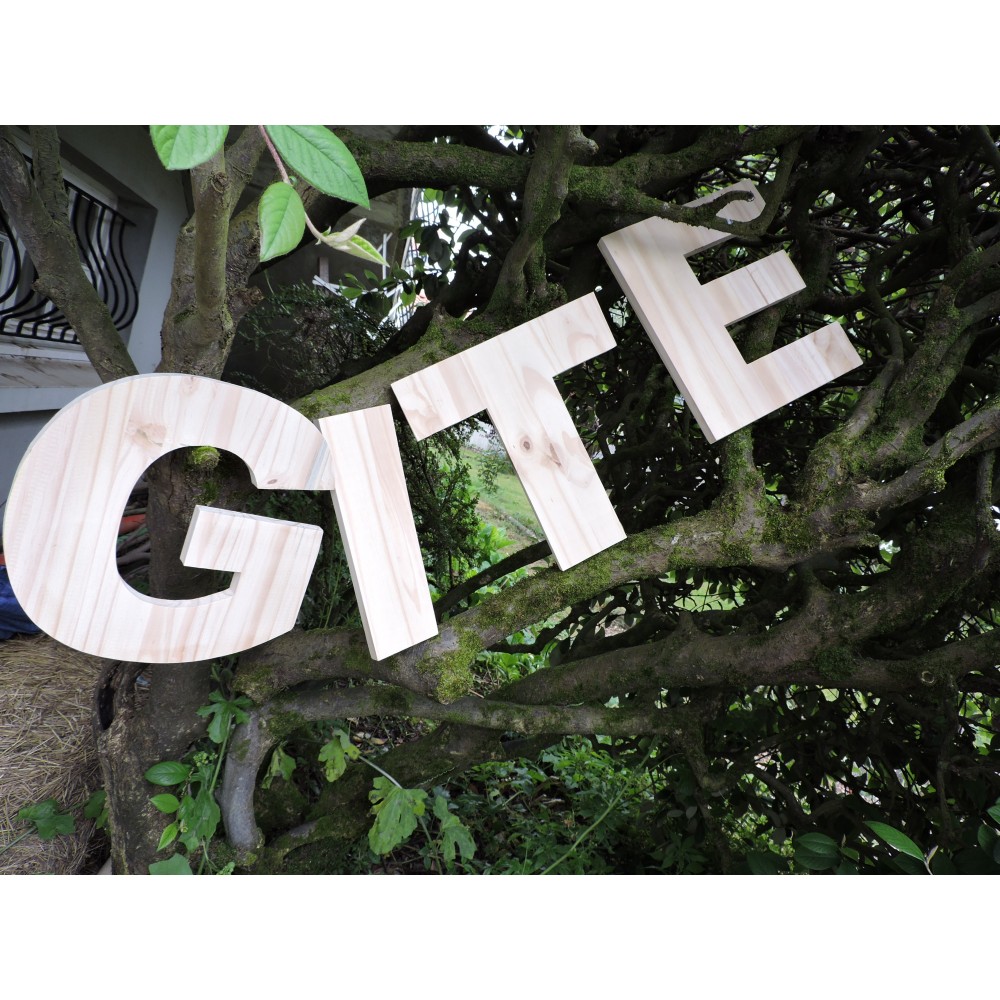 Lettres en bois géantes posées dans un arbre. Forme le mot "gîte".