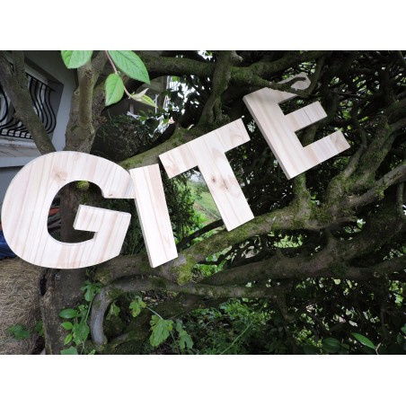 Lettres en bois géantes posées dans un arbre. Forme le mot "gîte".